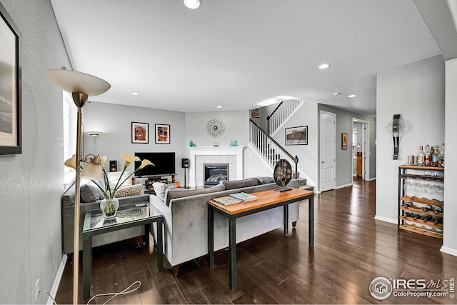 living area featuring recessed lighting, dark wood-style floors, stairs, and a tile fireplace