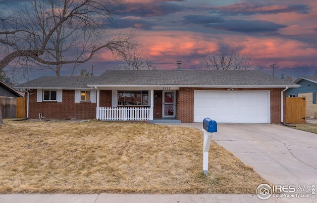 single story home featuring an attached garage, covered porch, concrete driveway, a front lawn, and brick siding