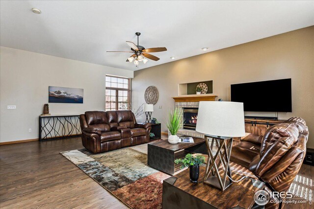 living room with a warm lit fireplace, baseboards, a ceiling fan, and wood finished floors