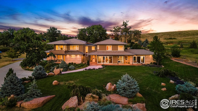 back of property at dusk with a lawn, covered porch, and driveway