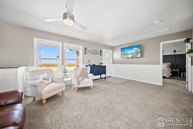 sitting room with a wainscoted wall, a ceiling fan, visible vents, and carpet flooring