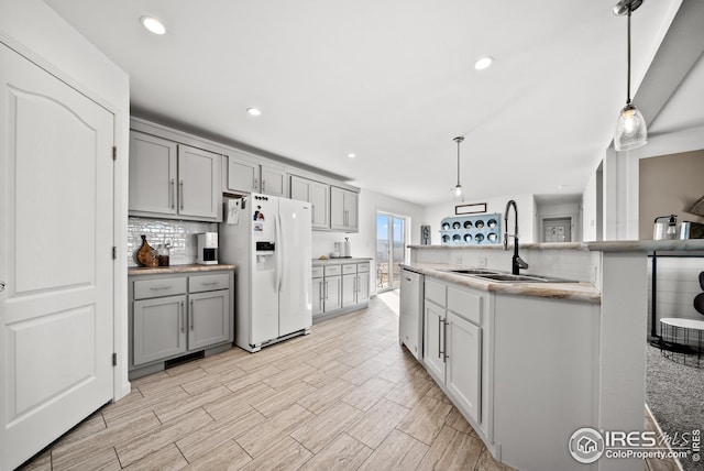 kitchen featuring backsplash, gray cabinets, stainless steel dishwasher, white fridge with ice dispenser, and a sink