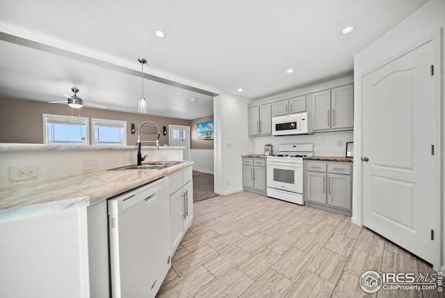 kitchen featuring white appliances, decorative light fixtures, gray cabinetry, and a sink