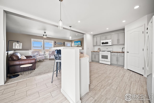 kitchen featuring white appliances, a breakfast bar, gray cabinets, pendant lighting, and open floor plan