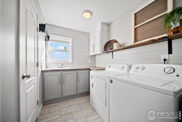 washroom with a sink, cabinet space, wooden walls, and independent washer and dryer