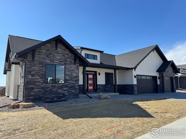 view of front of house featuring stone siding, an attached garage, driveway, and roof with shingles