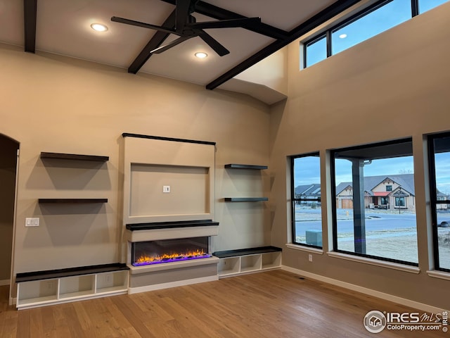 unfurnished living room featuring baseboards, ceiling fan, recessed lighting, a warm lit fireplace, and wood finished floors