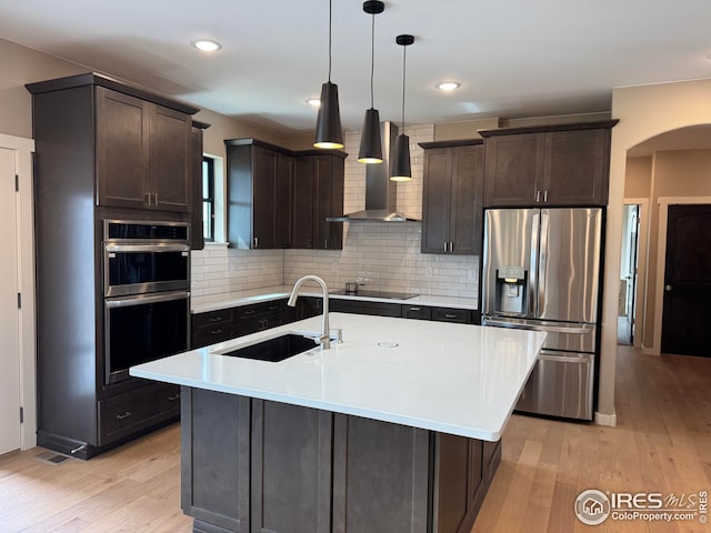 kitchen with light wood-style flooring, a sink, stainless steel appliances, dark brown cabinetry, and wall chimney exhaust hood