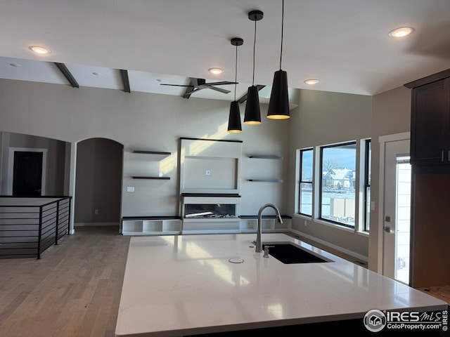 kitchen featuring a sink, recessed lighting, light wood-style floors, baseboards, and hanging light fixtures