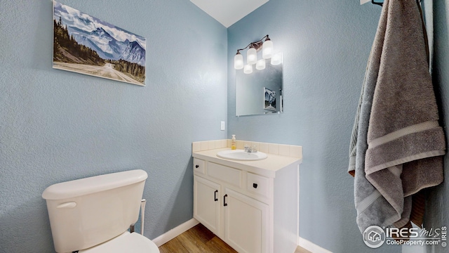 bathroom featuring toilet, wood finished floors, vanity, and a textured wall