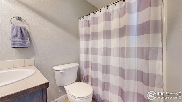 full bath featuring toilet, curtained shower, vanity, and a textured wall