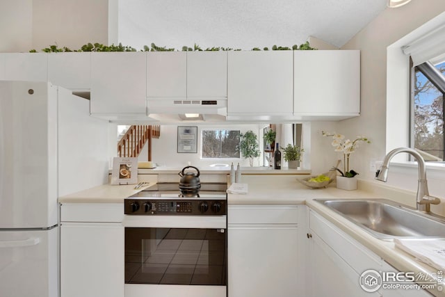 kitchen with range with electric cooktop, a sink, under cabinet range hood, white cabinetry, and freestanding refrigerator