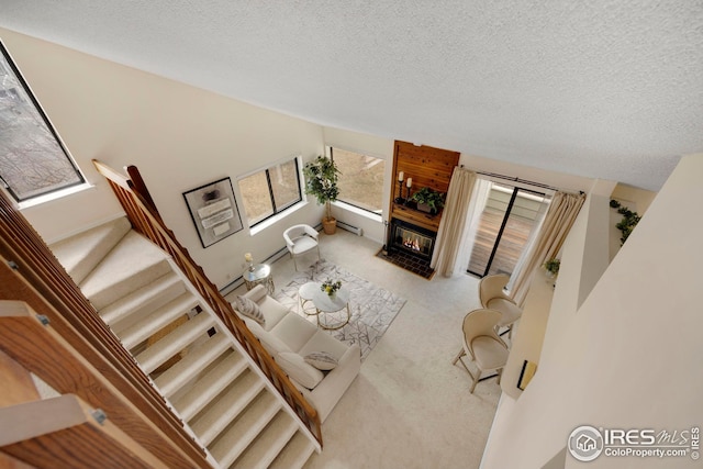 carpeted living area with stairway, a textured ceiling, and a glass covered fireplace