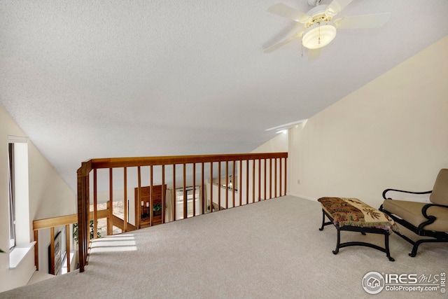 living area with ceiling fan, vaulted ceiling, carpet flooring, and a textured ceiling