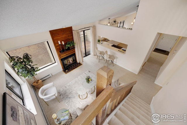 living room with carpet, a glass covered fireplace, a textured ceiling, high vaulted ceiling, and a baseboard radiator