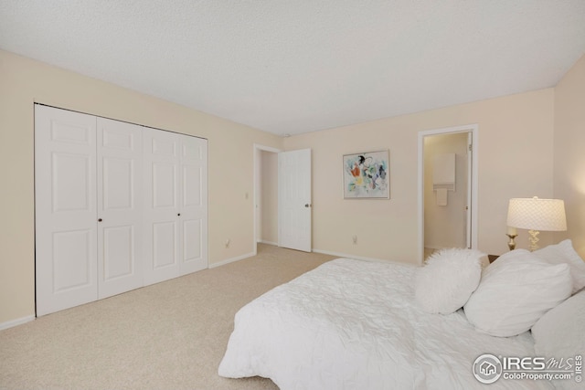 bedroom with a closet, light carpet, a textured ceiling, and baseboards