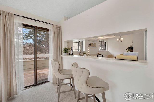 interior space featuring a wealth of natural light, a notable chandelier, a breakfast bar area, and carpet flooring