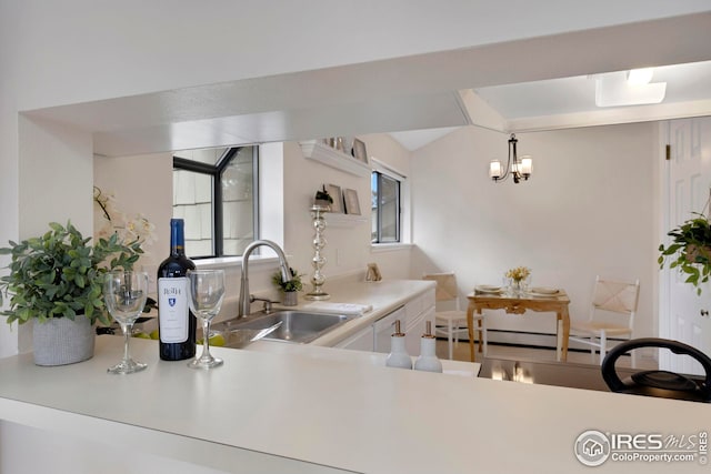 kitchen featuring a sink, a baseboard heating unit, an inviting chandelier, white cabinets, and light countertops