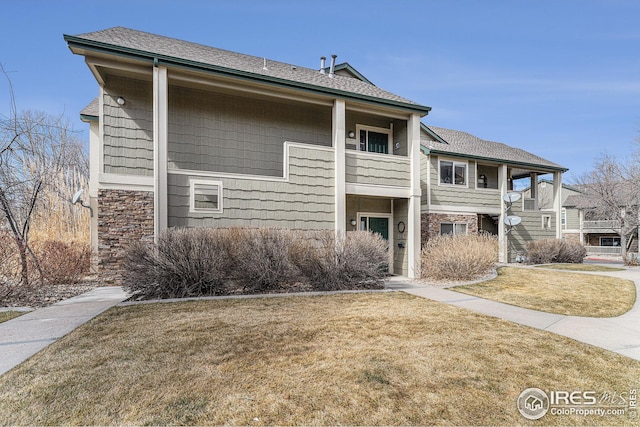 view of front of property with stone siding, a balcony, and a front lawn