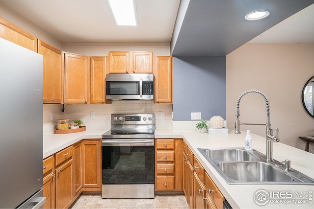 kitchen featuring a sink, tasteful backsplash, stainless steel appliances, a peninsula, and light countertops