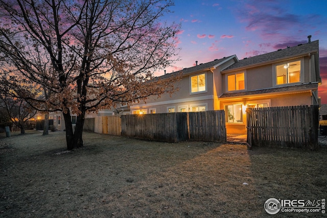 rear view of property featuring stucco siding, fence private yard, and a lawn