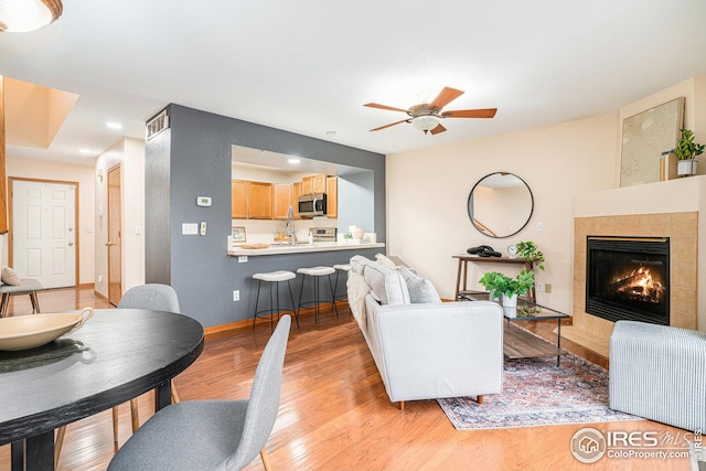 living area featuring light wood-type flooring, baseboards, ceiling fan, and a tile fireplace