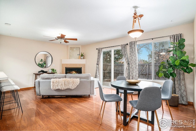 dining room with baseboards, a ceiling fan, wood finished floors, and a fireplace