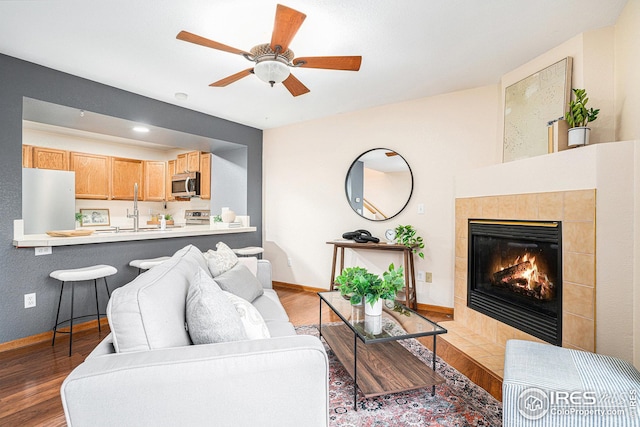 living area featuring a tiled fireplace, ceiling fan, light wood-type flooring, and baseboards