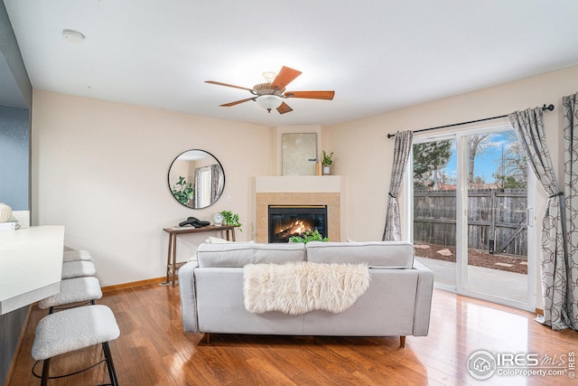 living area with ceiling fan, baseboards, wood finished floors, and a tiled fireplace