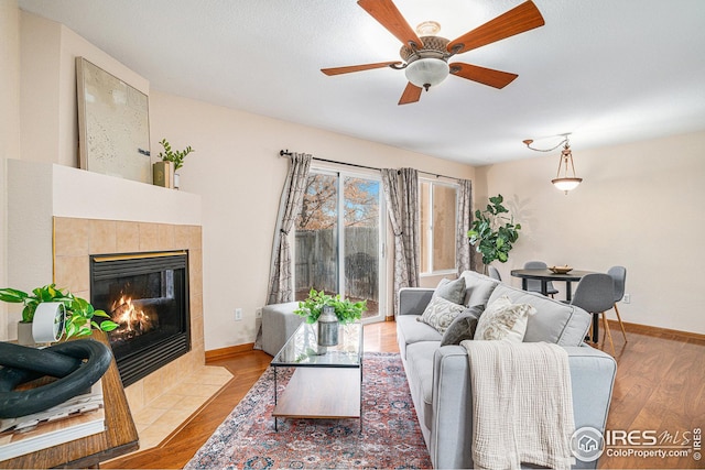 living room with ceiling fan, a fireplace, baseboards, and wood finished floors