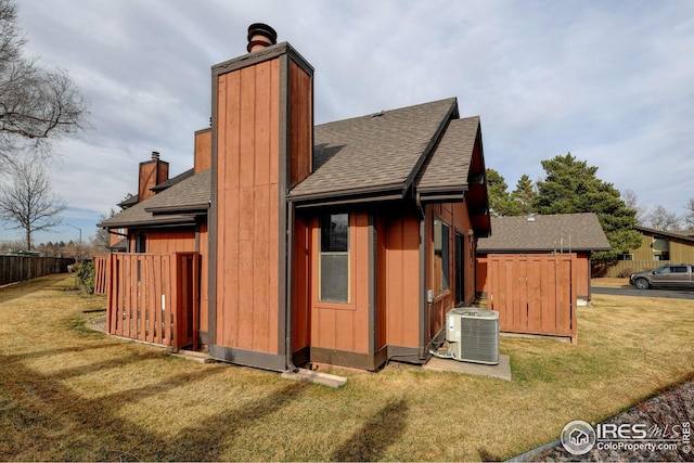 rear view of property featuring cooling unit, a yard, roof with shingles, and a chimney