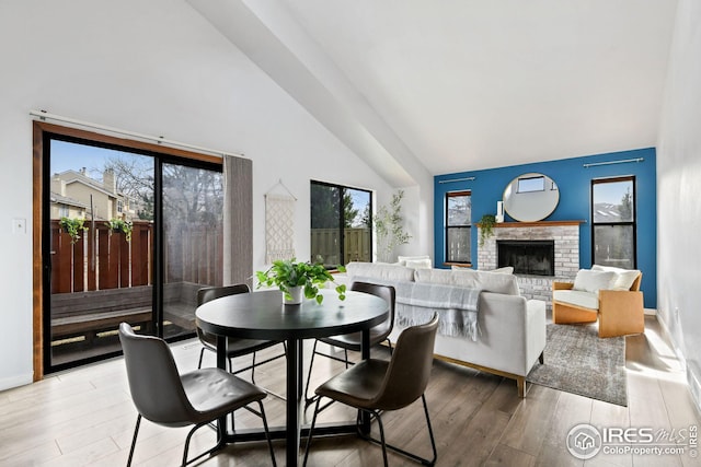 dining area featuring baseboards, high vaulted ceiling, a brick fireplace, and light wood finished floors