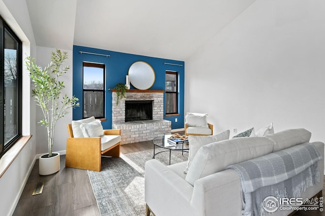 living area with visible vents, a brick fireplace, baseboards, vaulted ceiling, and wood finished floors