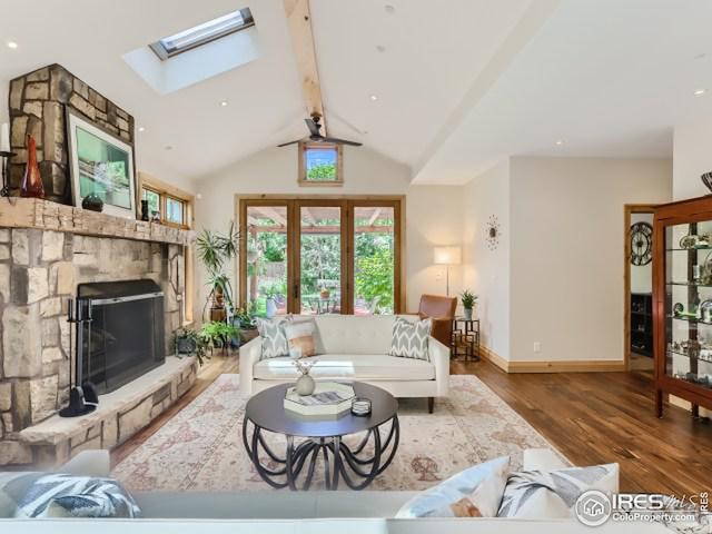 living room with a stone fireplace, vaulted ceiling with beams, wood finished floors, and baseboards