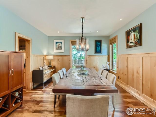 dining area with an inviting chandelier, wood finished floors, and a wainscoted wall