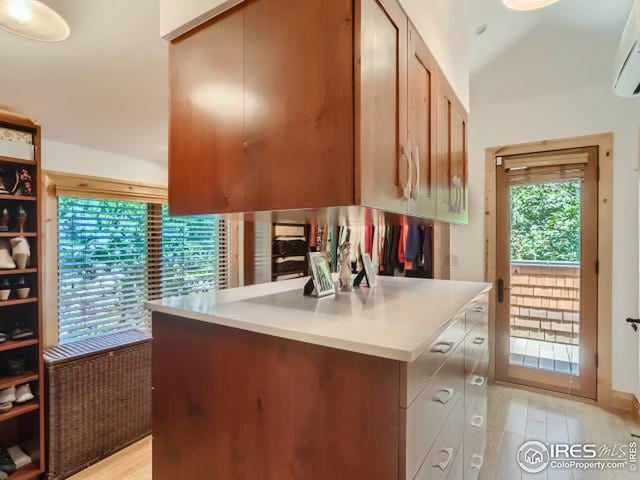 kitchen with light wood-type flooring, light countertops, lofted ceiling, and a wall unit AC