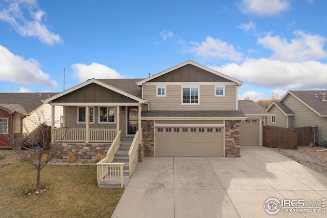 view of front of home with board and batten siding, fence, concrete driveway, covered porch, and stone siding