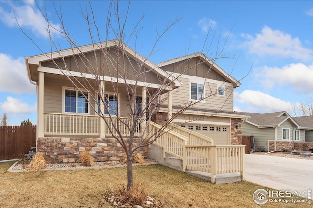 view of front of home with driveway, stone siding, fence, covered porch, and a garage