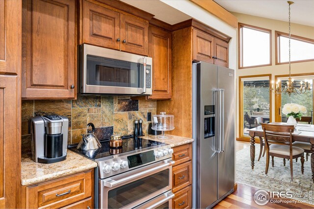kitchen featuring tasteful backsplash, a chandelier, light stone counters, appliances with stainless steel finishes, and brown cabinetry