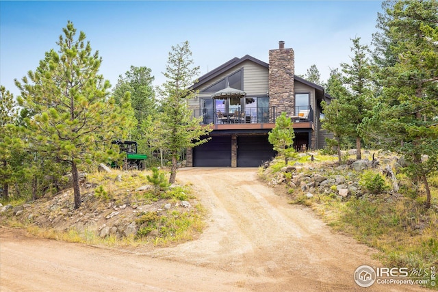 view of front of property with a chimney, a garage, stone siding, dirt driveway, and a deck