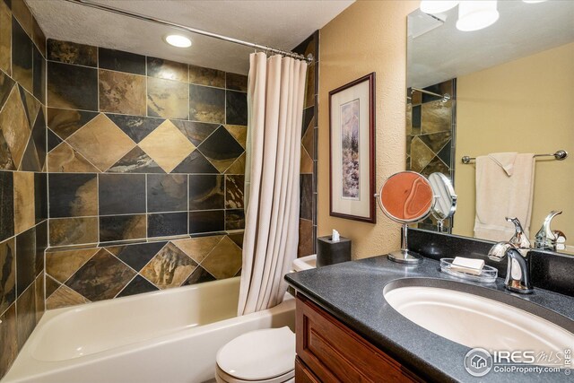 bathroom featuring toilet, vanity, a textured wall, and shower / bath combo