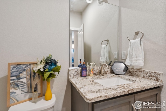 bathroom with toilet, vanity, and a textured wall