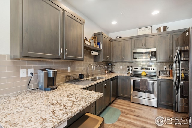 kitchen with light wood-style flooring, a sink, open shelves, stainless steel appliances, and light stone countertops