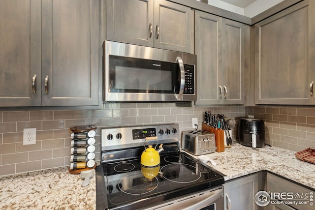 kitchen featuring backsplash, light stone countertops, and appliances with stainless steel finishes