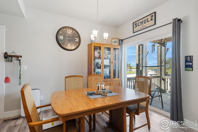 dining area featuring light wood finished floors, visible vents, baseboards, and a notable chandelier