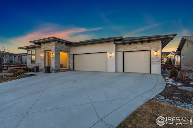 prairie-style home featuring concrete driveway, a garage, stone siding, and stucco siding