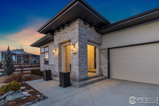 doorway to property featuring concrete driveway, stone siding, and stucco siding