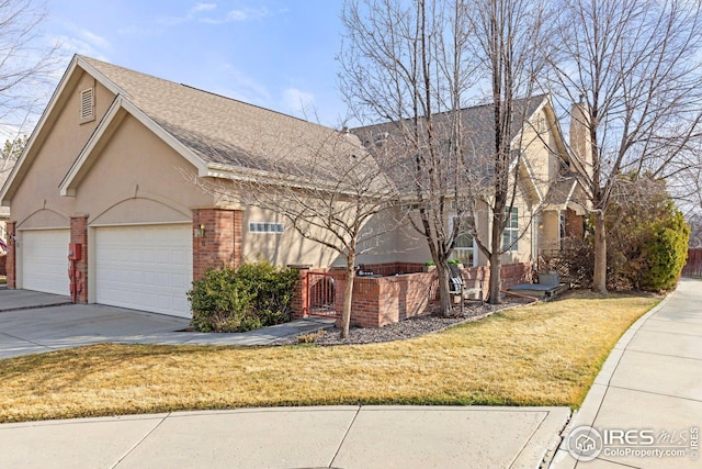 view of front of home with a shingled roof, stucco siding, concrete driveway, a front lawn, and brick siding