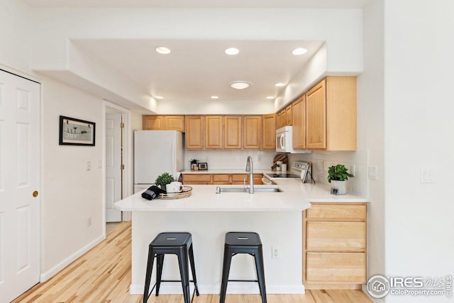 kitchen featuring white appliances, a peninsula, backsplash, and a sink