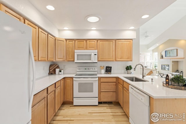 kitchen with backsplash, light wood-style flooring, a peninsula, white appliances, and a sink